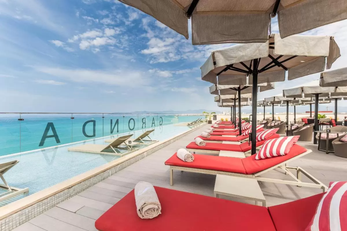 Terraza al aire libre con piscina de borde infinito y camastros con cojines rojos en Mallorca con vista panorámica al mar