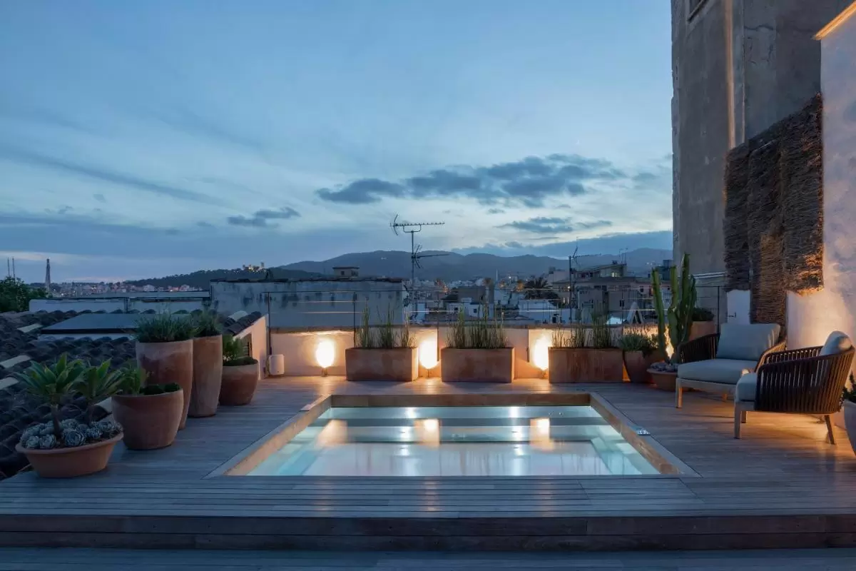 Terraza con jacuzzi empotrado, deck de madera y plantas iluminadas al atardecer en Mallorca
