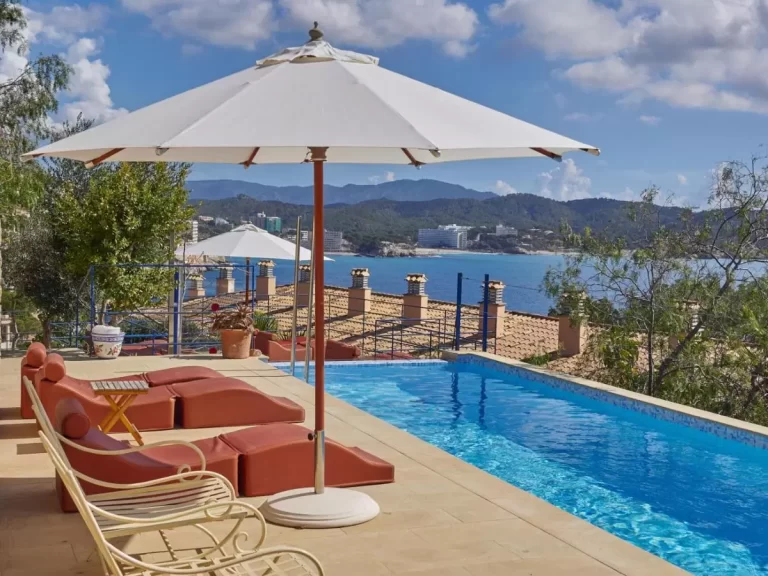 Terraza con piscina de borde infinito, tumbonas terracota y vistas panorámicas al mar y montañas en Mallorca