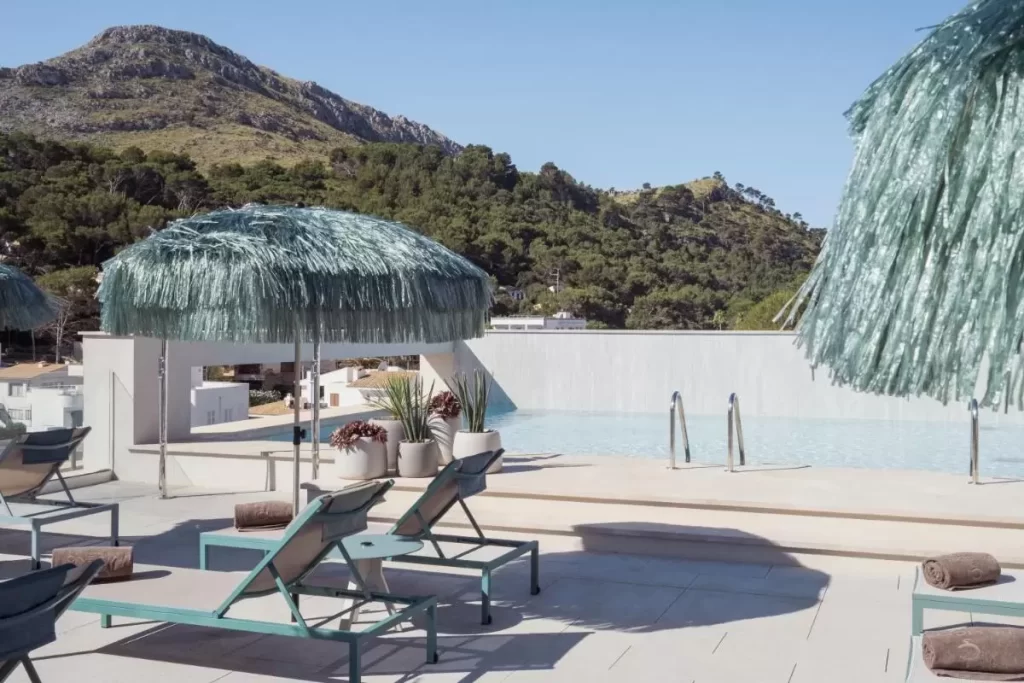Terraza con piscina elevada de borde infinito y tumbonas bajo sombrillas de flecos en Mallorca
