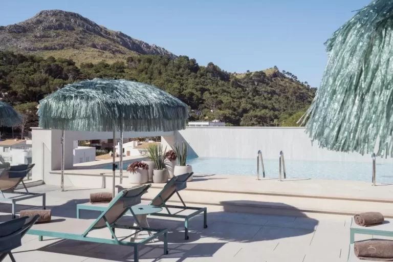 Terraza con piscina elevada de borde infinito y tumbonas bajo sombrillas de flecos en Mallorca