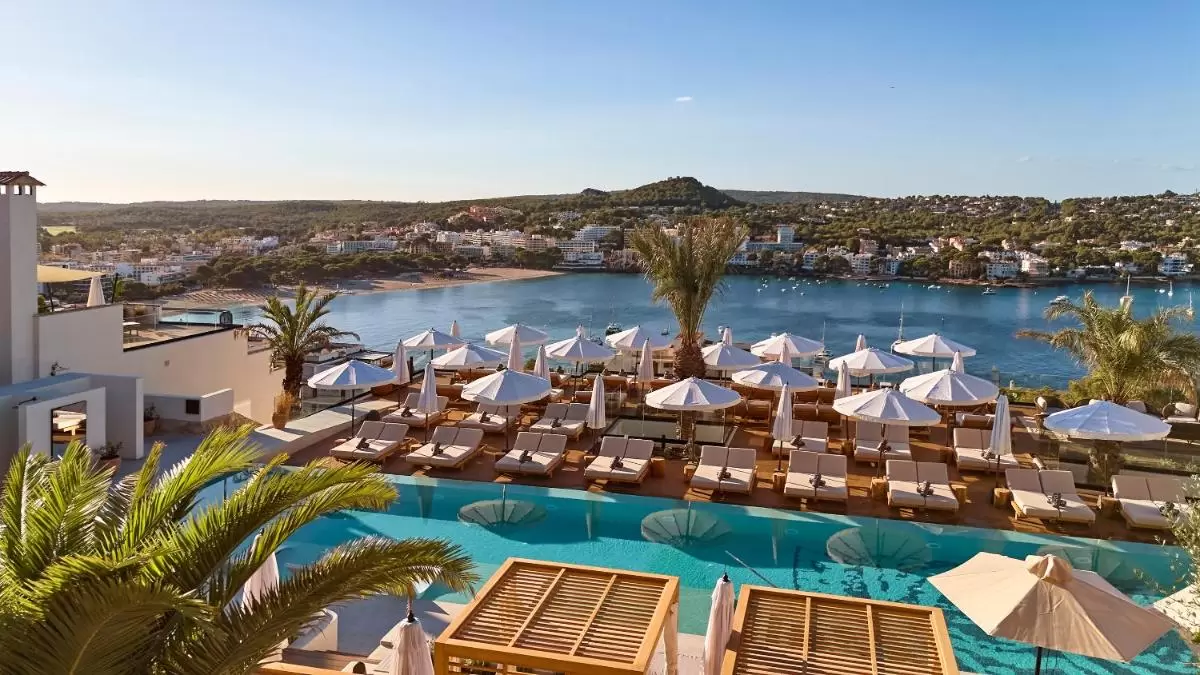 Terraza elevada con piscina alargada, tumbonas con sombrillas blancas y vistas a la bahía costera en Mallorca