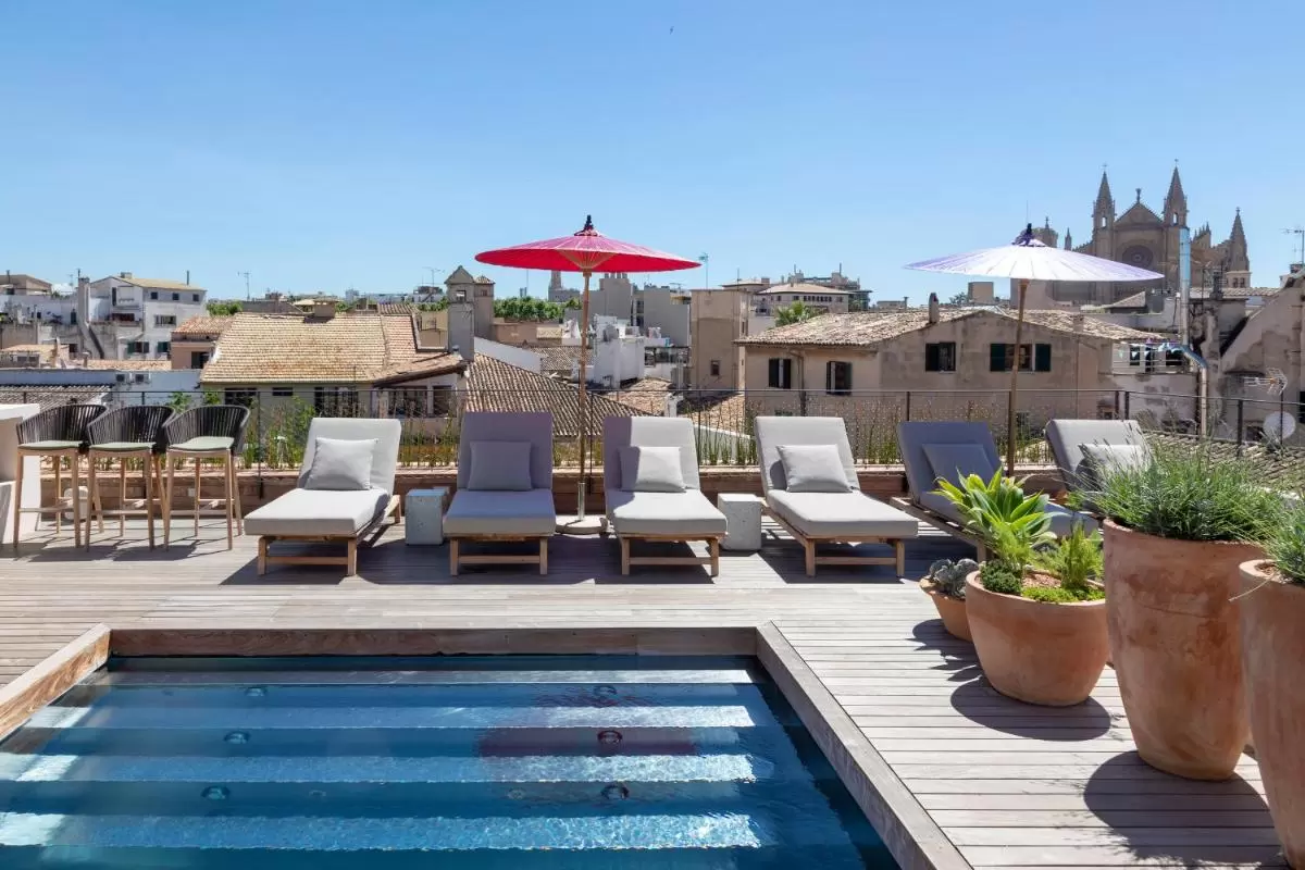 Terraza en Mallorca con piscina rectangular, tumbonas de madera y vista a arquitectura gótica tradicional