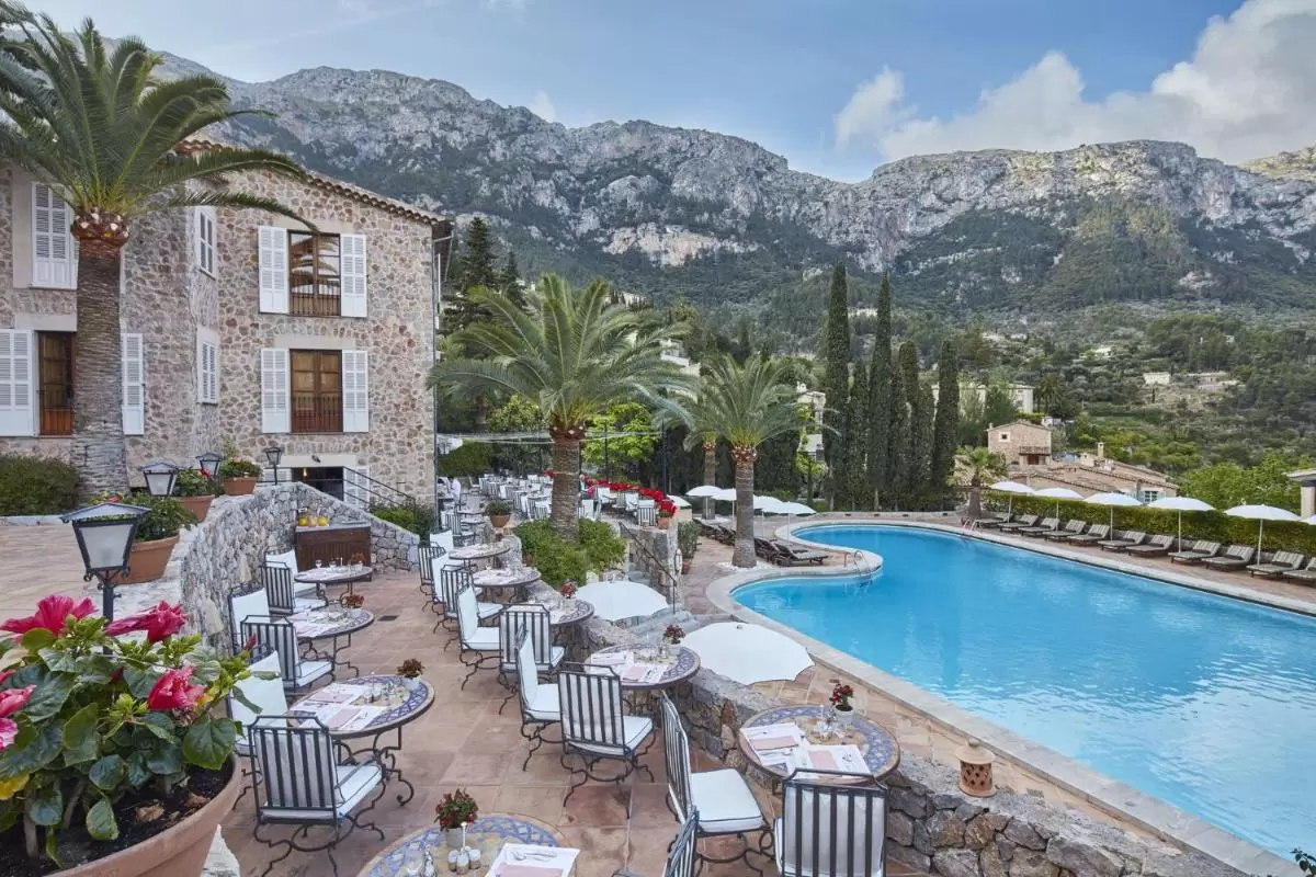 Terraza exterior con piscina irregular, mesas con mosaicos y vegetación mediterránea en entorno montañoso de Mallorca
