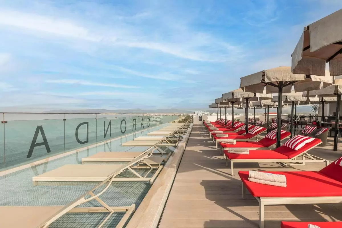 Terraza exterior con piscina y camastros rojos bajo sombrillas beige en Mallorca con vistas a montañas