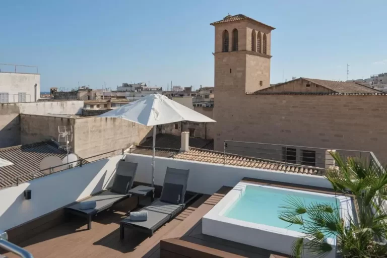 Terraza urbana en Mallorca con piscina pequeña, tumbonas y vistas a edificios históricos y modernos
