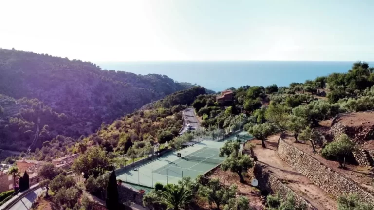 Vista aérea de paisaje montañoso en Mallorca con cancha de tenis, vegetación y carretera cerca del mar
