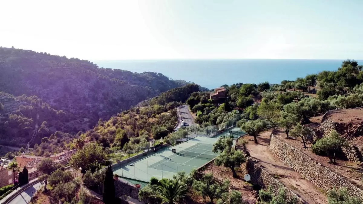 Vista aérea de paisaje montañoso en Mallorca con cancha de tenis, vegetación y carretera cerca del mar