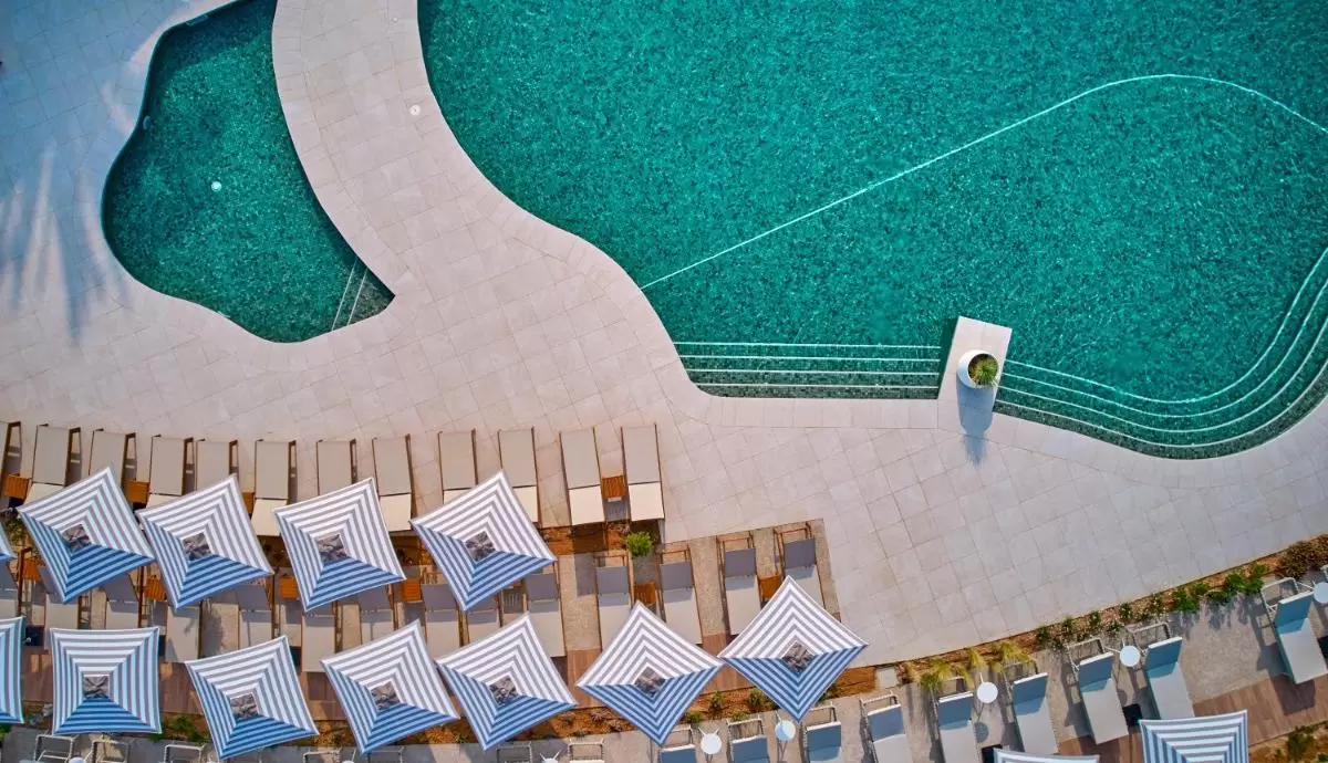 Vista aérea de piscina irregular con tumbonas y sombrillas a rayas en entorno exterior soleado en Mallorca