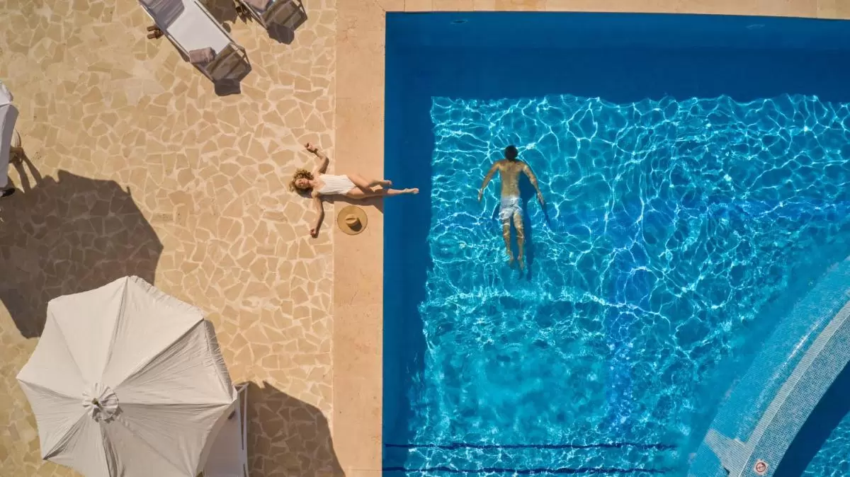 Vista aérea de piscina rectangular con hombre nadando y mujer descansando junto a jacuzzi en Mallorca
