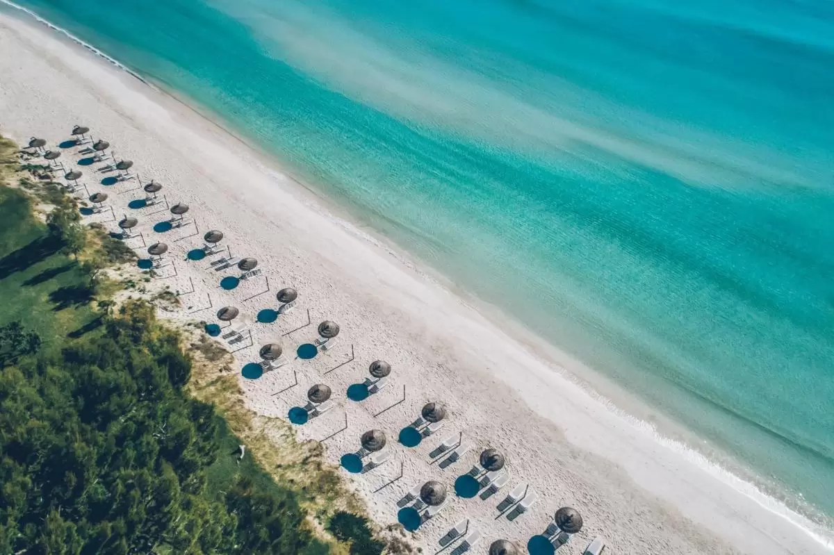 Vista aérea de playa en Mallorca con arena blanca, sombrillas de paja y tumbonas junto al mar turquesa transparente