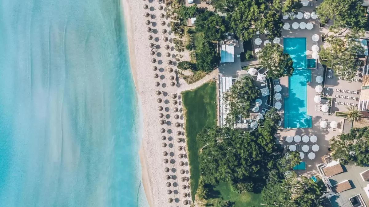Vista aérea de zona costera en Mallorca con playa, piscina, sombrillas y áreas verdes organizadas para descanso