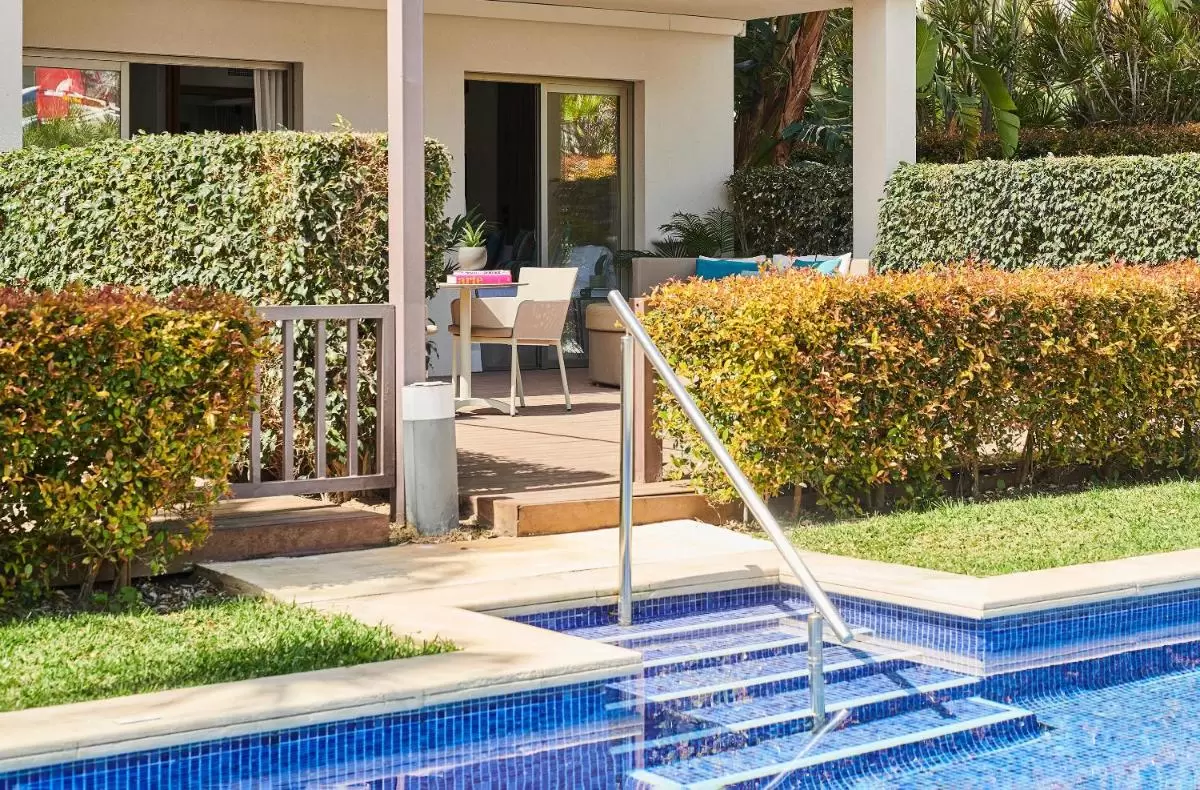 Zona exterior con piscina azul, porche cubierto y jardín cuidado en vivienda de Mallorca con acceso directo al agua
